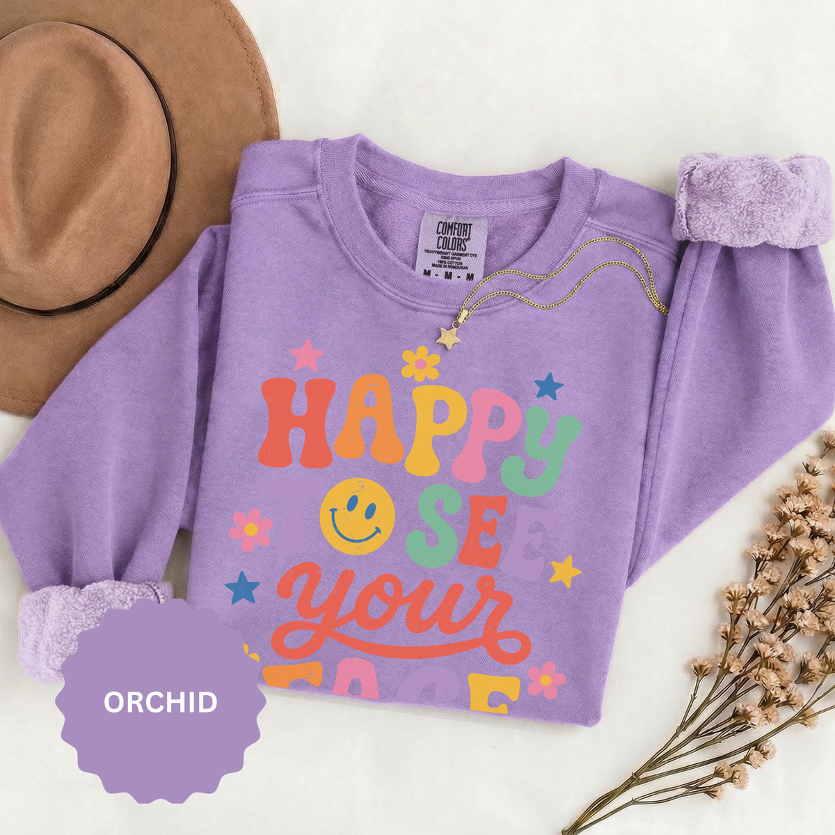 A purple crewneck sweatshirt printed with Happy to See Your Face in retro rainbow lettering with a smiley face and stars.