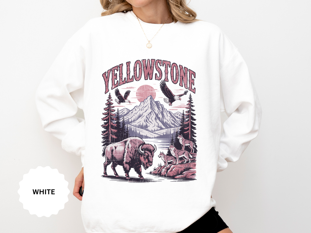 A white crewneck sweatshirt printed with Yellowstone above a mountain scene with a bison, wolves and eagles under a red sun.