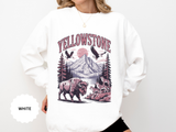 A white crewneck sweatshirt printed with Yellowstone above a mountain scene with a bison, wolves and eagles under a red sun.