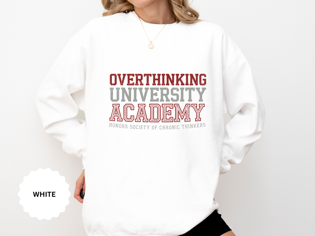 A white crewneck sweatshirt printed with Overthinking University Academy in red and gray varsity lettering and Honors Society of Chronic Thinkers.