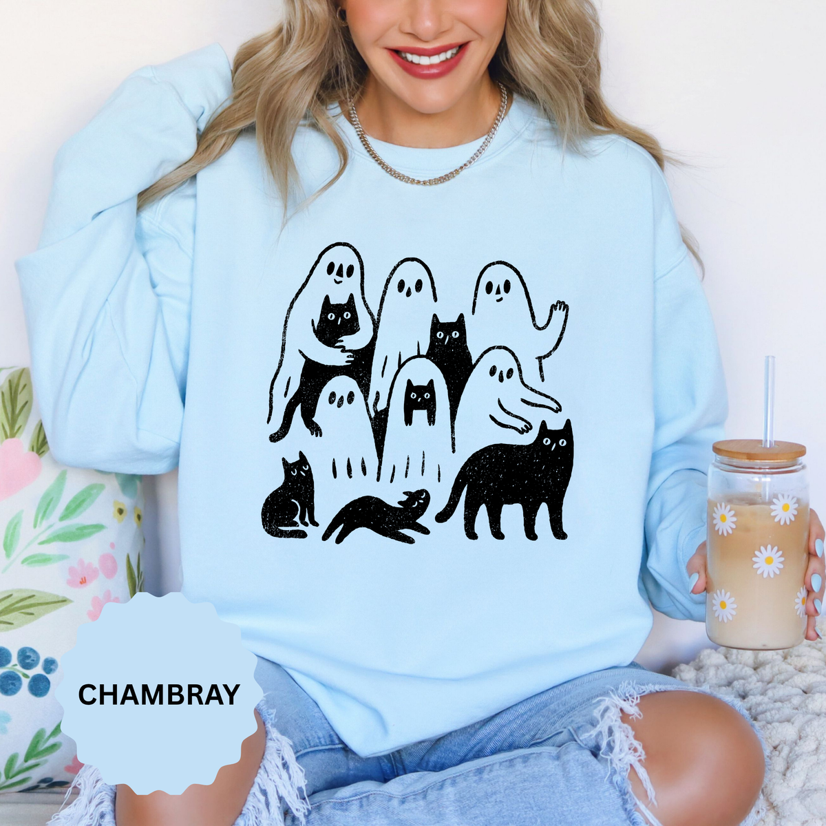 A light blue crewneck sweatshirt printed with a black line drawing of ghosts and cats playing together.