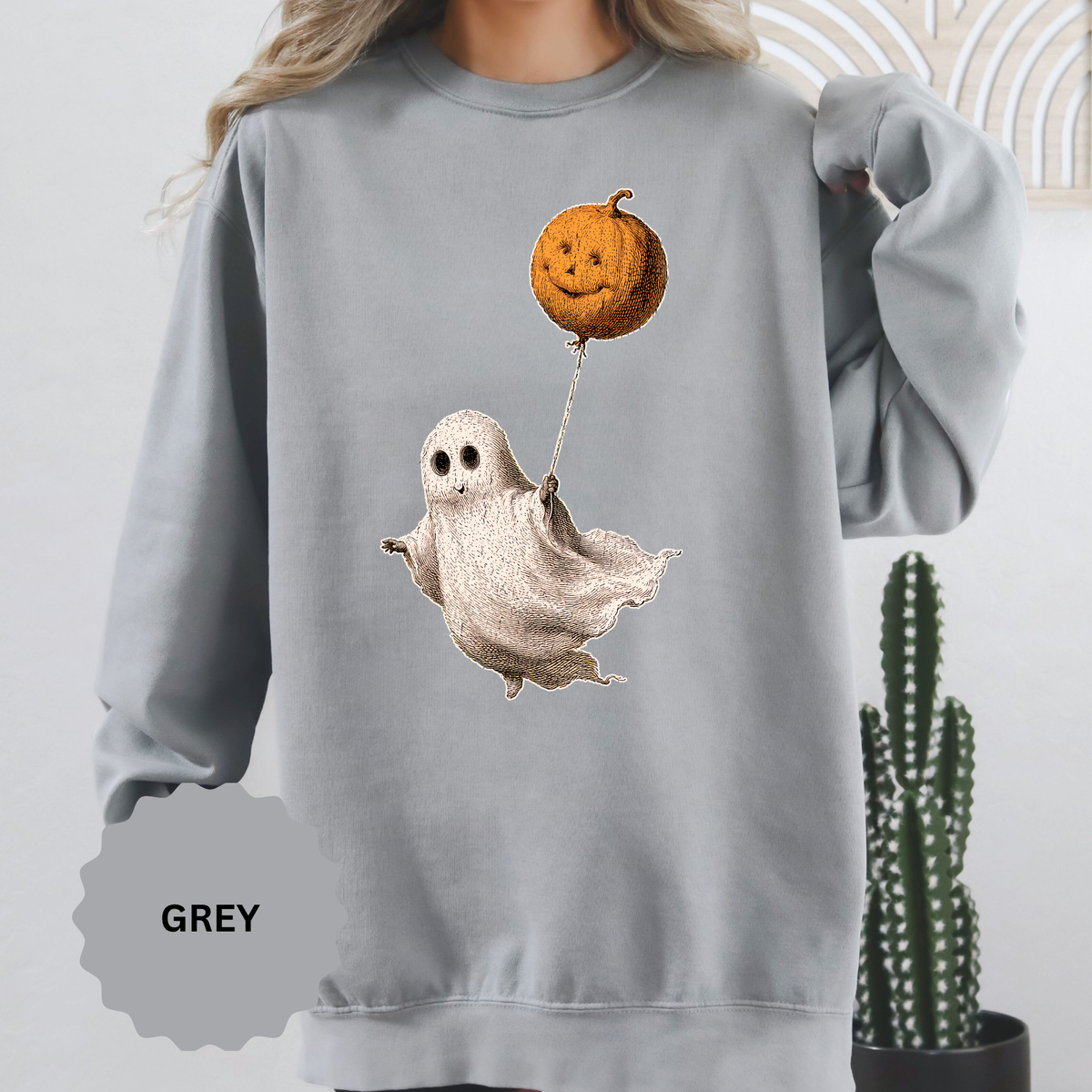 A gray crewneck sweatshirt printed with a vintage-style ghost floating while holding a jack-o'-lantern balloon.