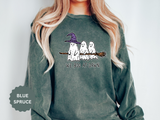 A green crewneck sweatshirt printed with three ghosts, one in a purple witch hat, sitting on a broomstick above the words We Boo at Dawn.