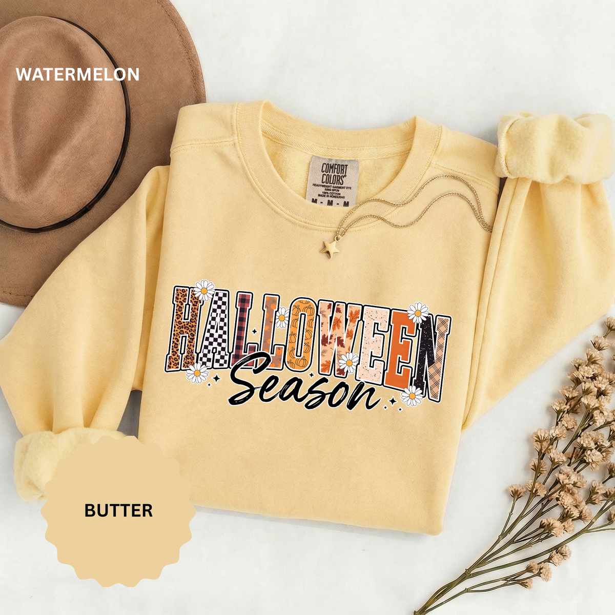 A pale yellow crewneck sweatshirt printed with HALLOWEEN in patchwork letters of leopard, checkerboard and plaid above Season in black script.