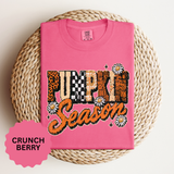 A pink T-shirt printed with PUMPKIN in leopard, checkerboard and paisley letters above Season in orange script with daisies.