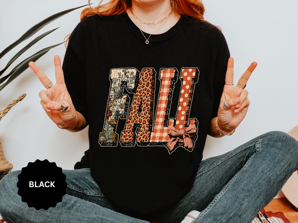 A black T-shirt printed with FALL in patchwork letters of camouflage, leopard, orange gingham and polka dots with a bow.