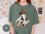 A green T-shirt printed with a ghost in a black-and-white cow-print sheet wearing a brown cowboy hat.