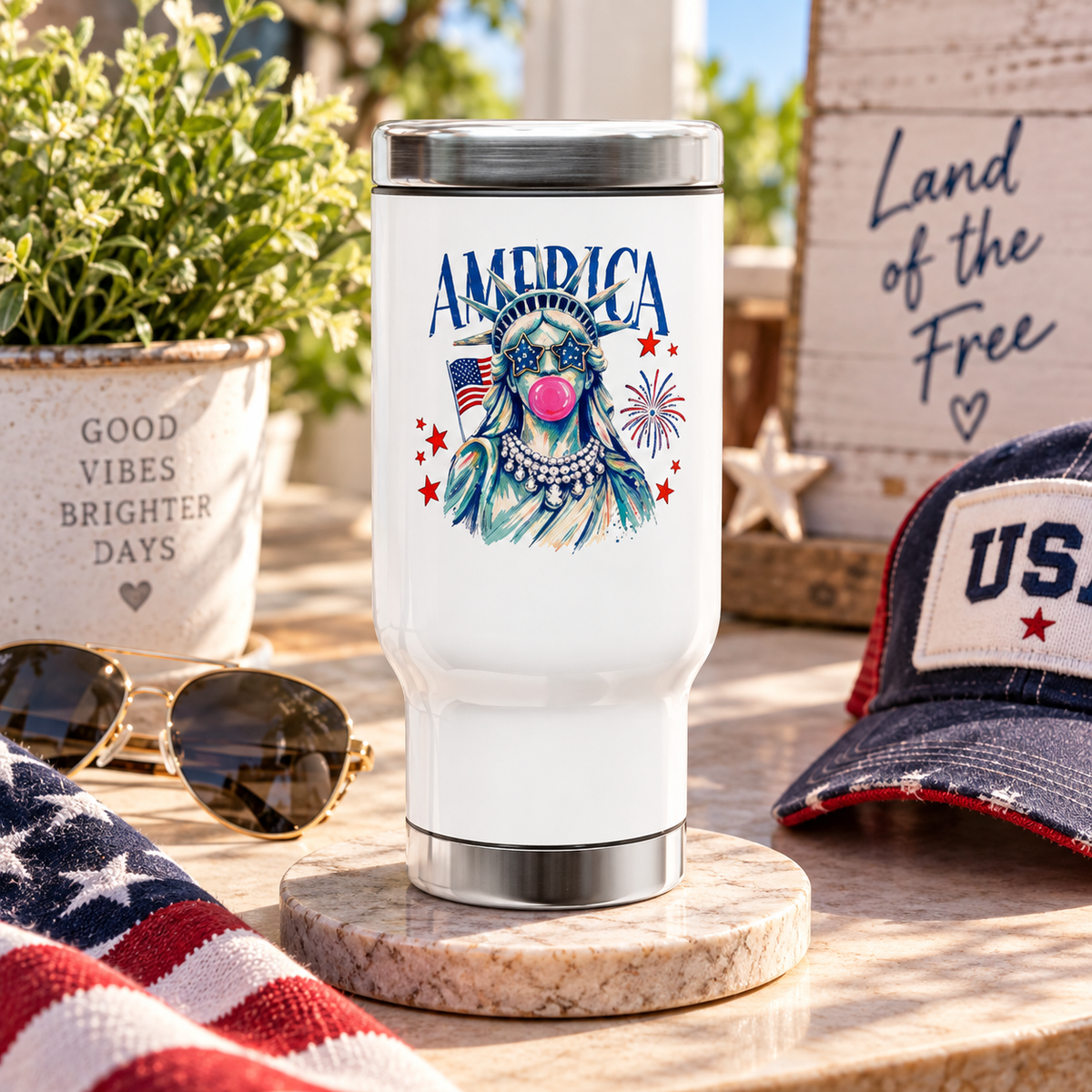 White stainless steel travel mug printed with 'AMERICA' text above an illustrated Statue of Liberty wearing star sunglasses, with a flag and fireworks.