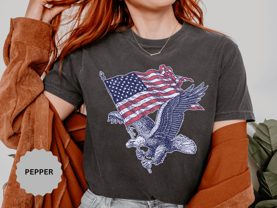 A dark gray T-shirt printed with a bald eagle in flight carrying a waving American flag.