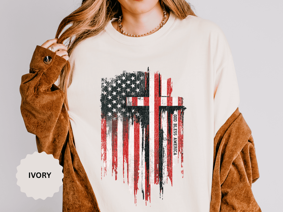 A cream T-shirt printed with a distressed American flag with two black crosses and the words God Bless America.
