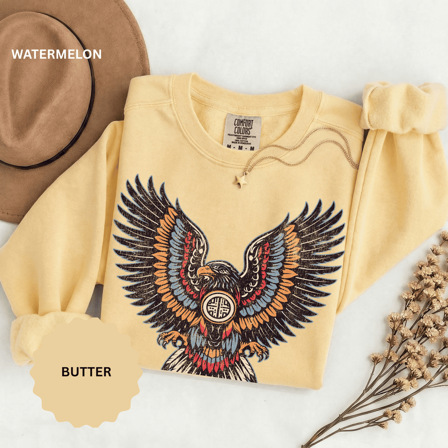 A pale yellow crewneck sweatshirt printed with an ornamental eagle with spread wings in red, blue and orange patterned feathers.