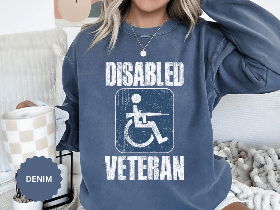 A blue crewneck sweatshirt printed with a distressed accessibility-symbol figure holding a rifle between Disabled and Veteran.