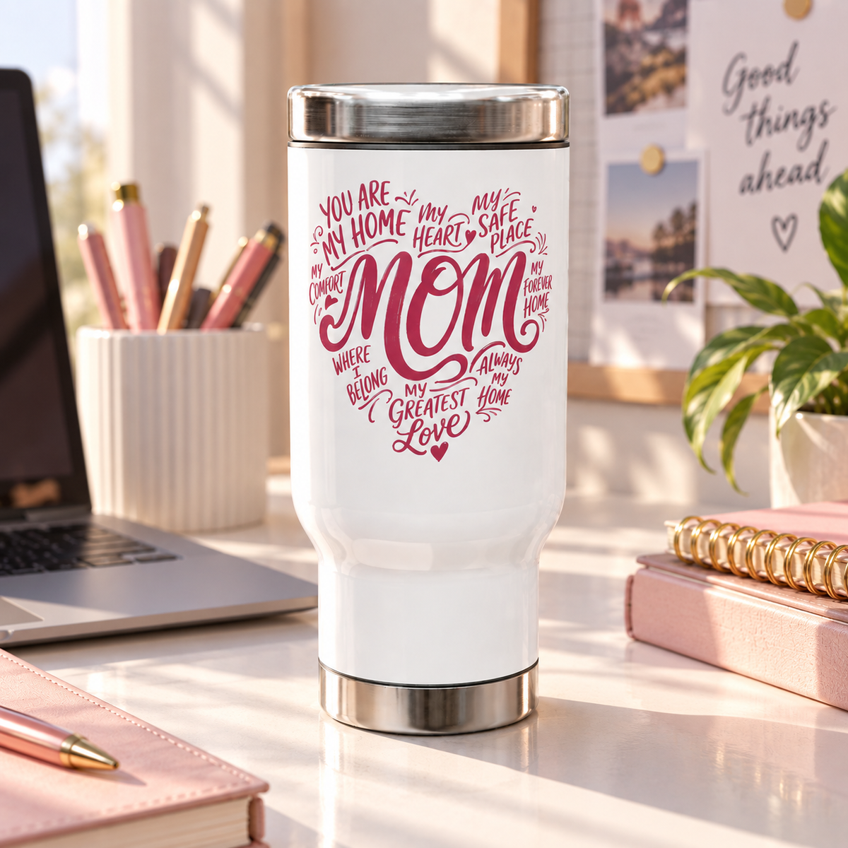 A white stainless steel travel mug with a screw-on lid, printed with a pink heart-shaped word design reading "MOM" and phrases like "my greatest love", on a desk.