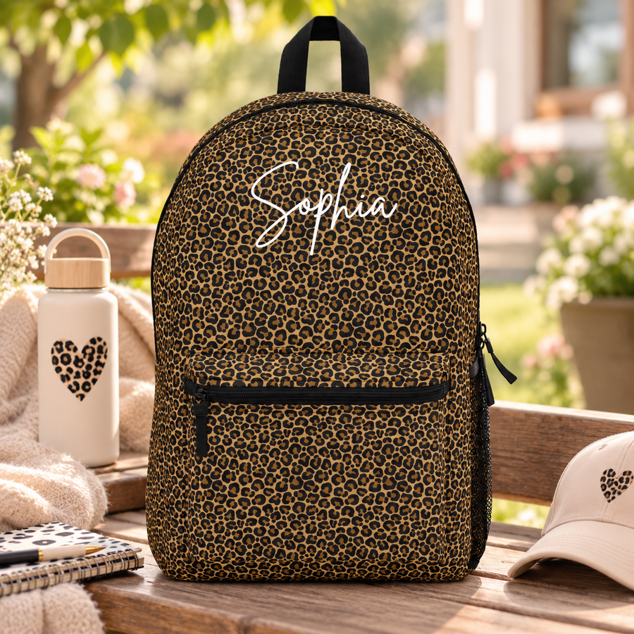 A backpack with black top handle, front zip pocket and mesh side pocket, covered in an all-over brown and black leopard print, with the sample name "Sophia" in white script across the top.