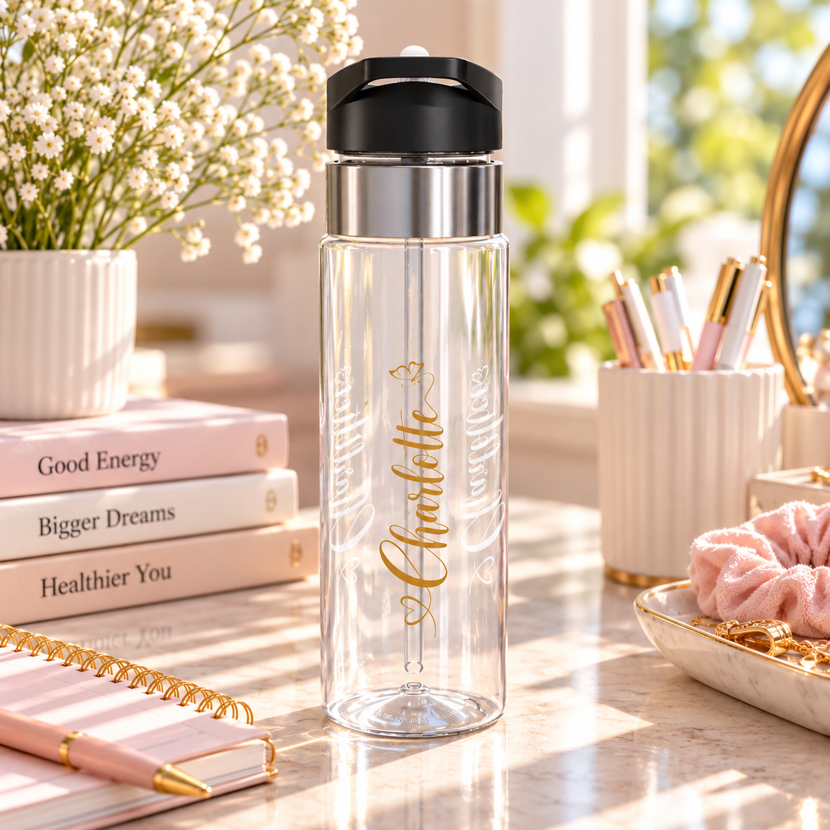 A clear water bottle with a black flip-top lid, stainless band and straw, printed with the sample name "Charlotte" in vertical gold script with two small gold butterflies.