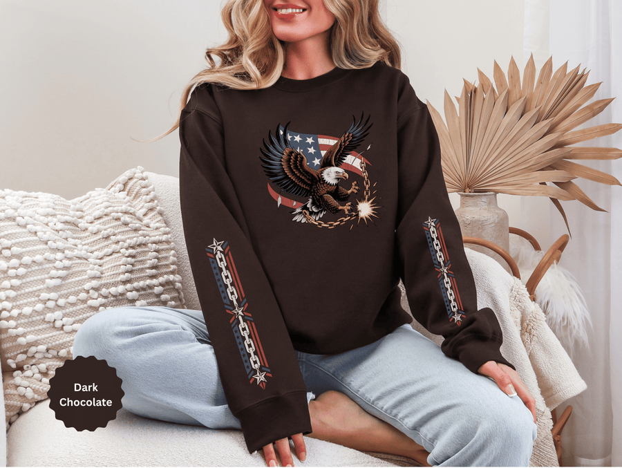 A woman wearing a dark brown crewneck sweatshirt printed with an eagle breaking a chain in front of an American flag, with chain designs down both sleeves.