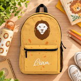 A backpack with a black top handle, front zip pocket and mesh side pocket, mustard yellow with orange speckles, a large brown and white lion face and the sample name "Liam" in white script on the pocket.