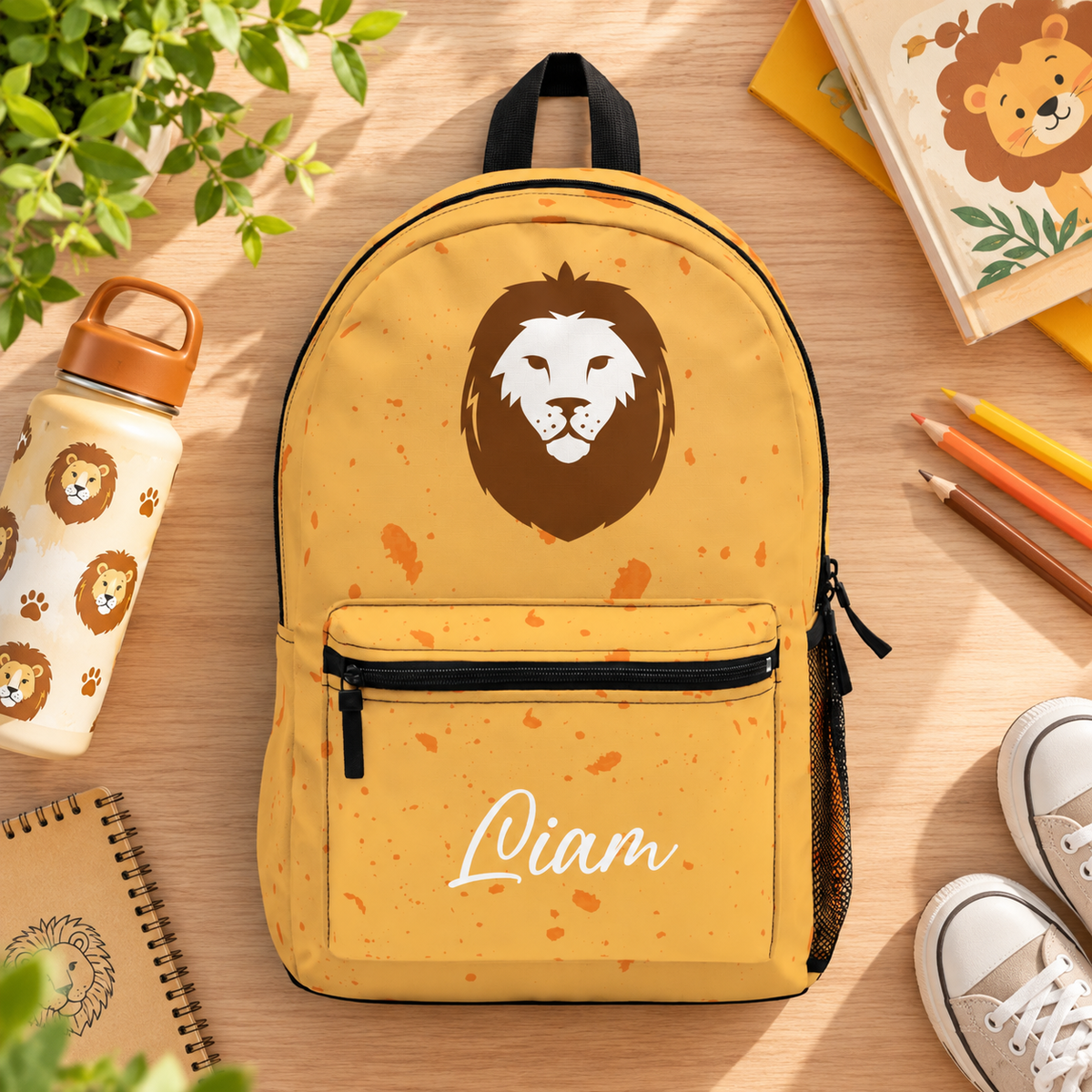 A backpack with a black top handle, front zip pocket and mesh side pocket, mustard yellow with orange speckles, a large brown and white lion face and the sample name "Liam" in white script on the pocket.