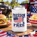 A white can cooler on a drink can, printed with "FREEDOM ISN'T FREE" in navy lettering around an American flag and a soldier's cross with helmet and boots.