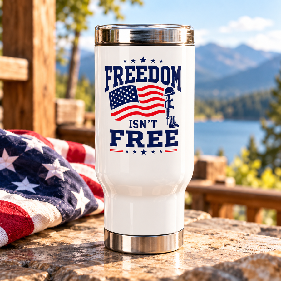 A white stainless steel travel mug with a silver lid and base, printed with "FREEDOM ISN'T FREE" in navy lettering around a waving American flag and a soldier's cross with helmet and boots.