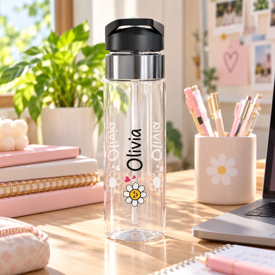 A clear water bottle with a black flip-top lid, stainless band and straw, printed with a smiling yellow and white daisy, small pink hearts and the sample name "Olivia" in black lettering.