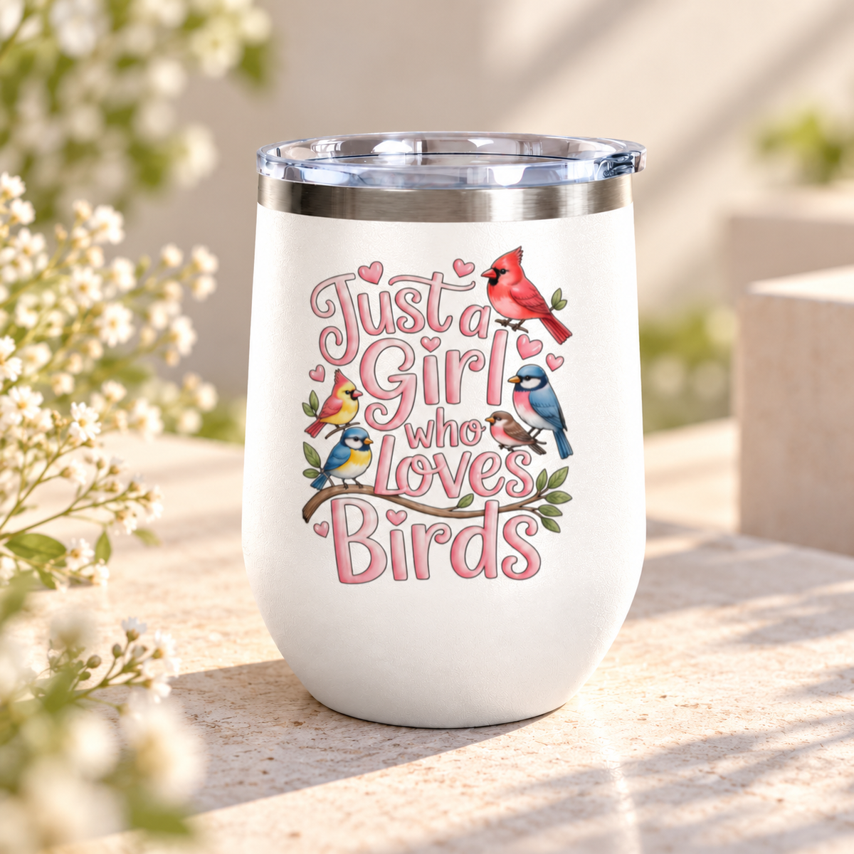 A white stainless steel stemless wine tumbler with a clear push-on lid, printed with "Just a Girl who Loves Birds" in pink bubble lettering with a cardinal, a blue jay, goldfinches and finches on a branch.