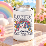 A white can cooler on a drink can, printed with "HOPING YOU HAVE A MAGICAL DAY!" around a cute unicorn on a cloud under a rainbow with stars and hearts.