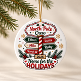 A round white ceramic Christmas ornament on a gold string, printed with "North Pole Crew" above a candy-cane signpost with five sample names, "2026" and "Home for the Holidays".