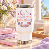 A white stainless steel travel mug with a silver lid and base, printed with "CREATE YOUR OWN MAGIC" in lilac and coral lettering under a crescent moon and a star wand, framed by butterflies, ribbons and flowers.