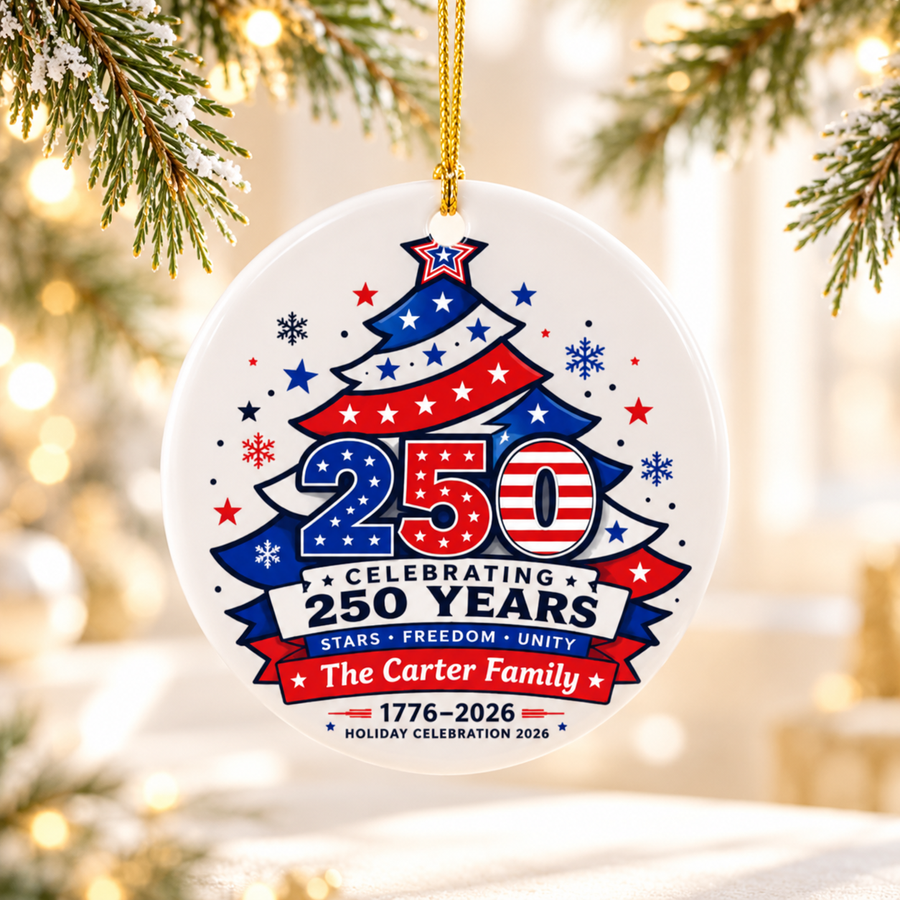 A round white ceramic Christmas ornament on a gold string, printed with a red, white and blue Christmas tree with stars, a large "250", "Celebrating 250 Years", a sample family name and "1776–2026".