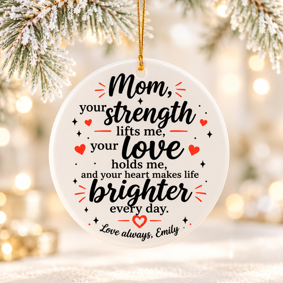 A round white ceramic Christmas ornament on a gold string, printed with a verse in black script, "Mom, your strength lifts me, your love holds me", with red hearts and a sample "Love always" signature.