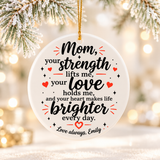 A round white ceramic Christmas ornament on a gold string, printed with a verse in black script, "Mom, your strength lifts me, your love holds me", with red hearts and a sample "Love always" signature.
