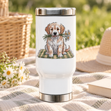 A white stainless steel travel mug with a silver lid and base, printed with a fluffy golden and cream puppy sitting on a green plaid blanket, holding white daisies in its mouth.