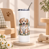 A white stainless steel skinny tumbler with a clear lid and metal straw, printed with a fluffy golden and cream puppy sitting on a green plaid blanket, holding white daisies in its mouth.