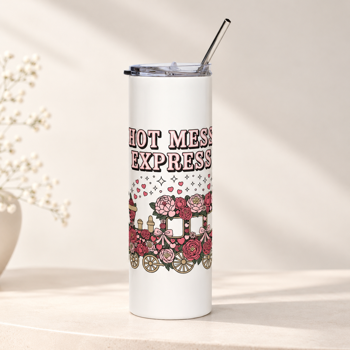 A white stainless steel skinny tumbler with a clear lid and metal straw, printed with "HOT MESS EXPRESS" in pink lettering above a steam train covered in pink and red roses and bows, with hearts and sparkles rising from it.