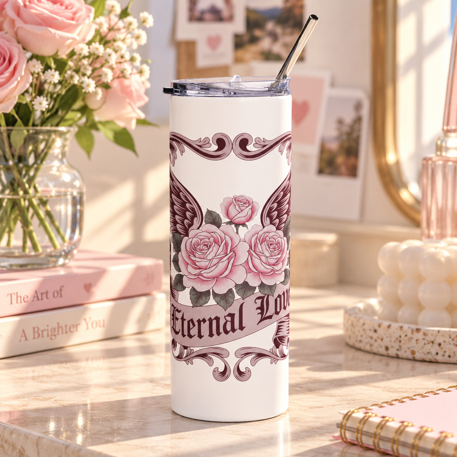 A white stainless steel skinny tumbler with a clear lid and metal straw, printed with pink roses in front of dark burgundy wings, framed by ornate vintage scrollwork, above a banner reading "Eternal Love".
