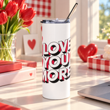A white stainless steel skinny tumbler with a clear lid and metal straw, printed with "I LOVE YOU MORE" in bold white block lettering with red and black drop shadows.