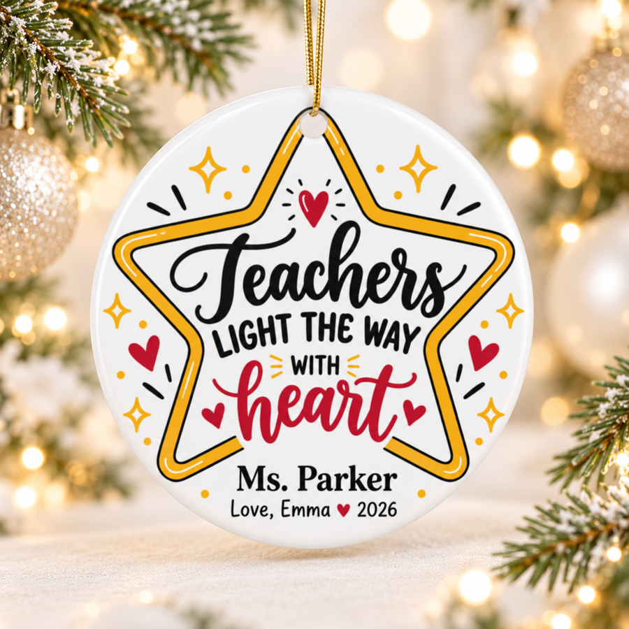A round white ceramic Christmas ornament on a gold string, printed with "Teachers LIGHT THE WAY WITH heart" in black and red script inside a gold star outline with sparkles and hearts, with a sample teacher name and a "Love" signature with "2026".