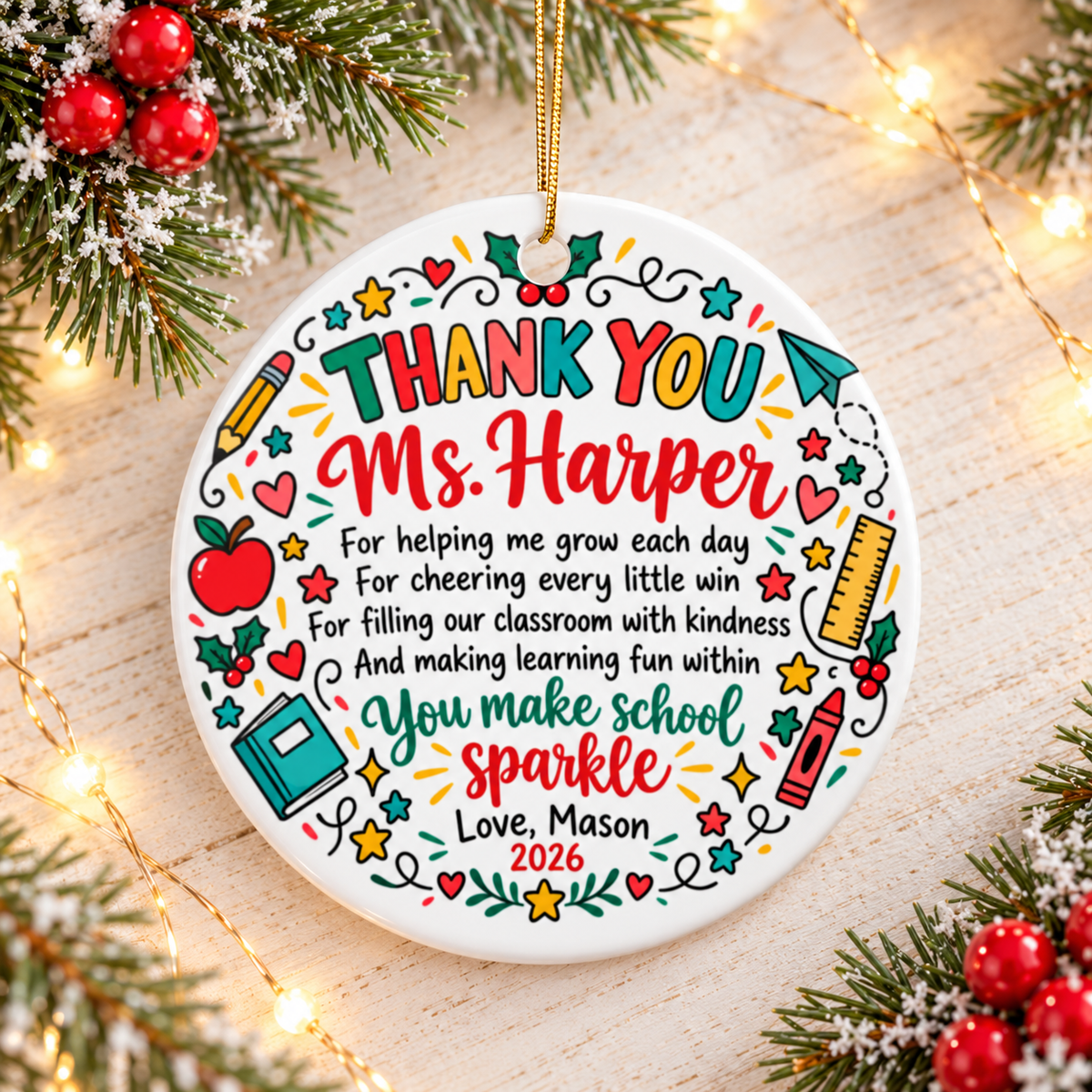 A round white ceramic Christmas ornament on a gold string, printed with "THANK YOU" in colorful letters above a sample teacher name and a short verse ending "You make school sparkle", framed by an apple, a book, a ruler, a crayon, a pencil, stars and holly, with a "Love" signature and "2026".