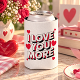 A white can cooler on a drink can, printed with "I LOVE YOU MORE" in bold white block lettering with red and black drop shadows, surrounded by red hearts.