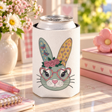 A white can cooler on a drink can, printed with a cute gray-green bunny face wearing pink heart-shaped glasses and a crown of pink roses, with butterfly and flower patterned ears.
