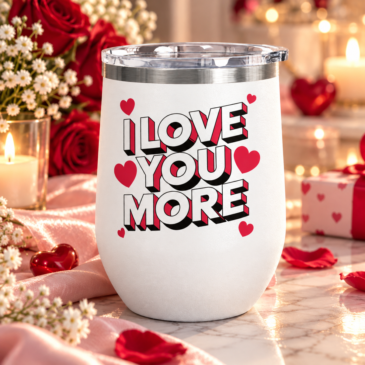 A white stainless steel stemless wine tumbler with a clear push-on lid, printed with "I LOVE YOU MORE" in bold white block lettering with red and black drop shadows, surrounded by red hearts.