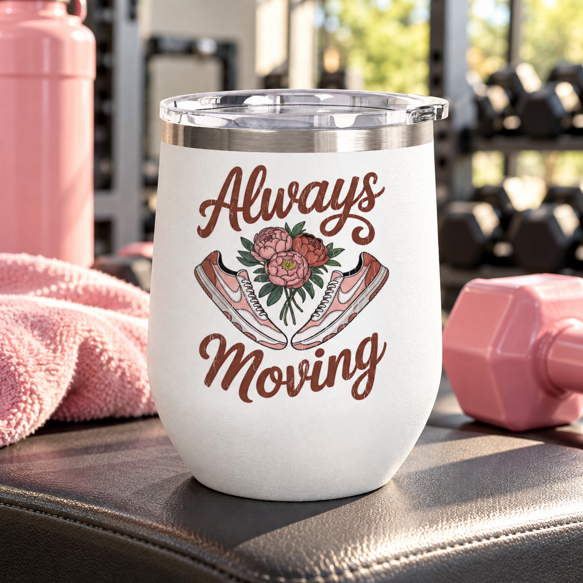 A white stainless steel stemless wine tumbler with a clear push-on lid, printed with "Always Moving" in brown script around a bouquet of pink peonies between a pair of pink and white sneakers.