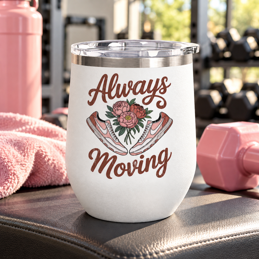 A white stainless steel stemless wine tumbler with a clear push-on lid, printed with "Always Moving" in brown script around a bouquet of pink peonies between a pair of pink and white sneakers.