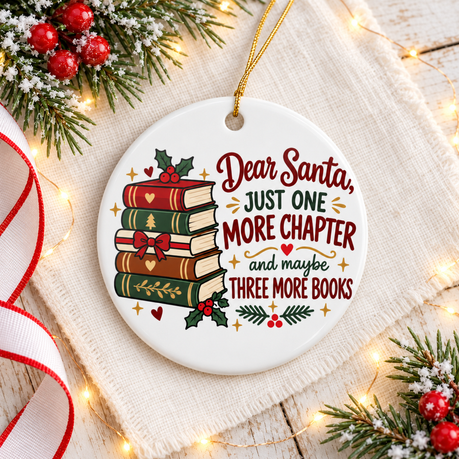 A round white ceramic Christmas ornament on a gold string, printed with a stack of red, green, cream and brown books with a red bow and holly beside "Dear Santa, JUST ONE MORE CHAPTER and maybe THREE MORE BOOKS" in red and green lettering.