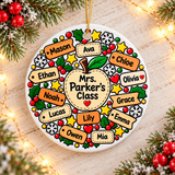 A round white ceramic Christmas ornament on a gold string, printed with a large apple reading a sample "Mrs. Parker's Class", ringed by orange and cream name tags with sample student names, holly, gold stars, snowflakes and red berries.