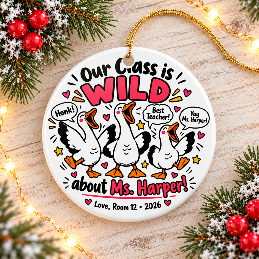 A round white ceramic Christmas ornament on a gold string, printed with "Our Class is WILD about" a sample teacher name in black and pink lettering around three cartoon white geese honking, with speech bubbles reading "Honk!", "Best Teacher!" and a cheer, hearts, stars and a room-number signature with "2026".