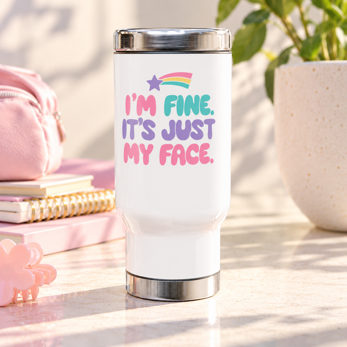 A white stainless steel travel mug with a silver lid and base, printed with "I'M FINE. IT'S JUST MY FACE." in pink, mint and lavender bubble letters under a rainbow shooting star.