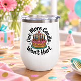 A white stainless steel stemless wine tumbler with a clear push-on lid, printed with "One More Candle Won't Hurt" in black script around a pink and yellow birthday cake with striped lit candles.