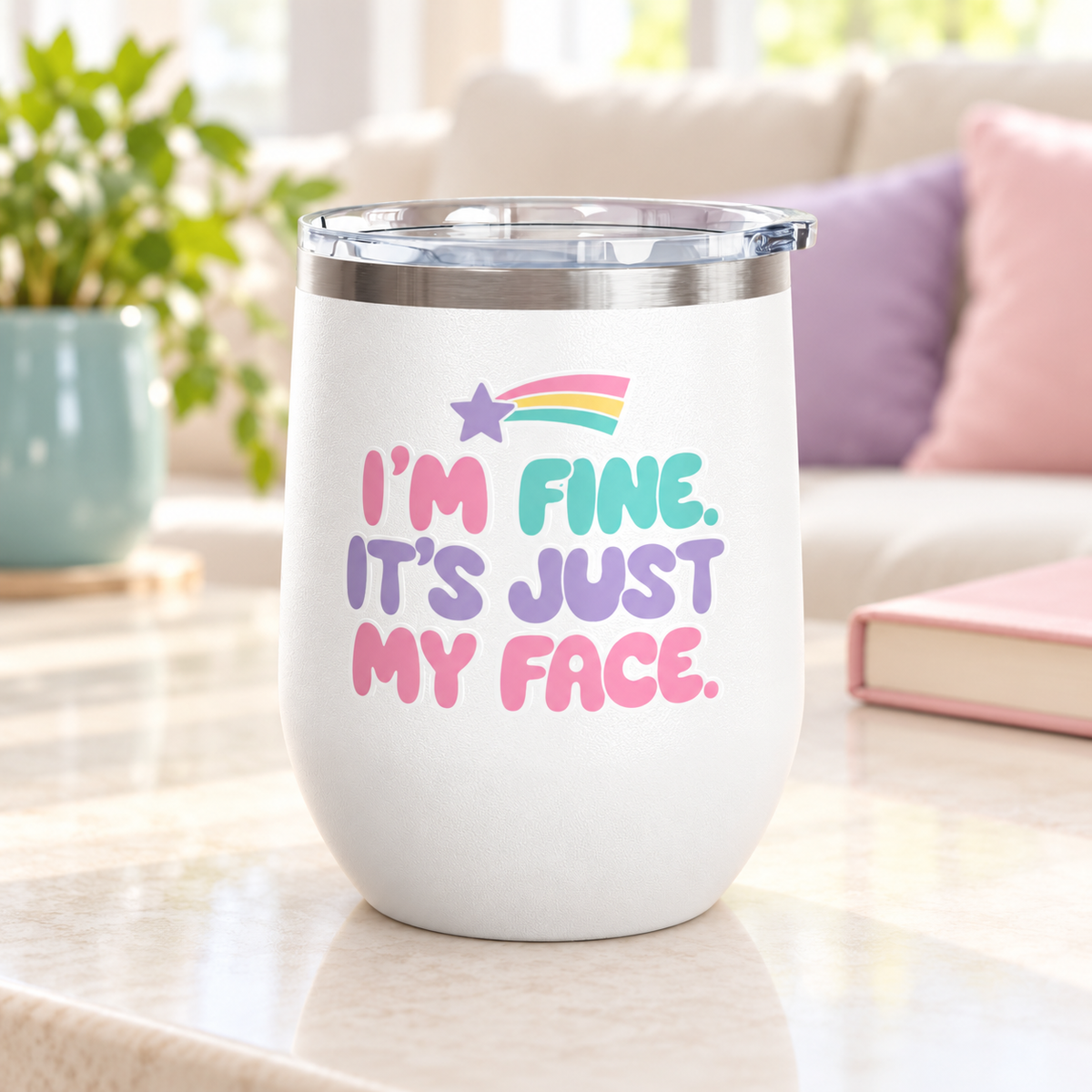 A white stainless steel stemless wine tumbler with a clear push-on lid, printed with "I'M FINE. IT'S JUST MY FACE." in pink, mint and lavender bubble letters under a rainbow shooting star.